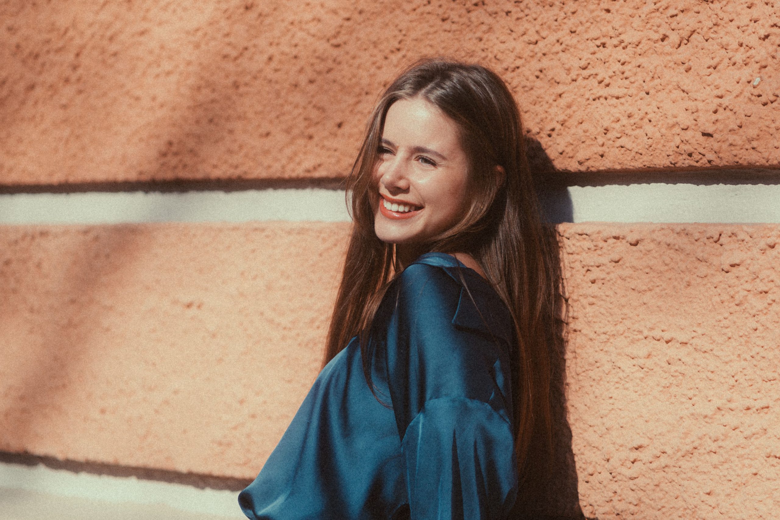 Jeune femme souriante en blouse devant mur rouge