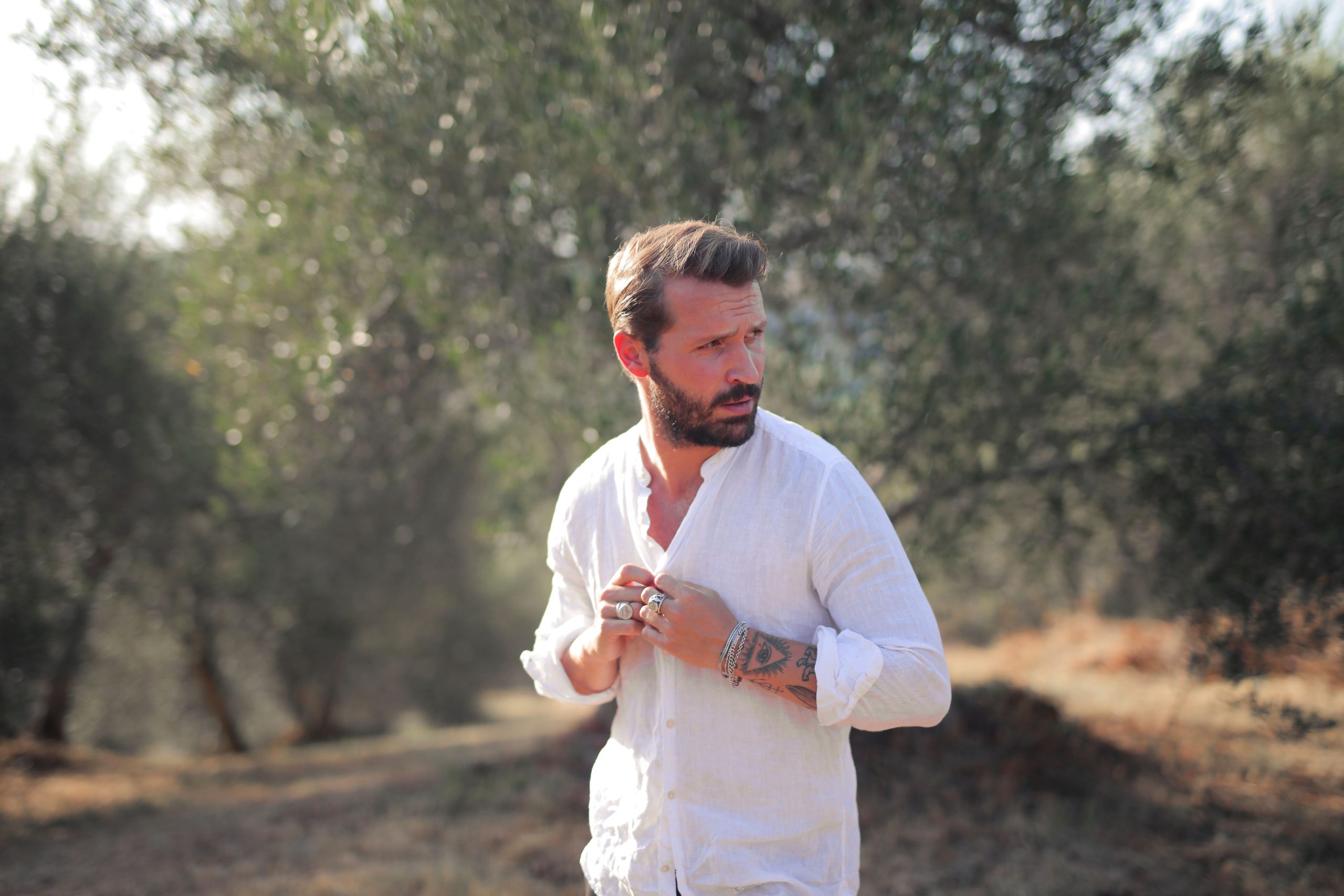 Homme barbu en chemise blanche décontracté dans une oliveraie