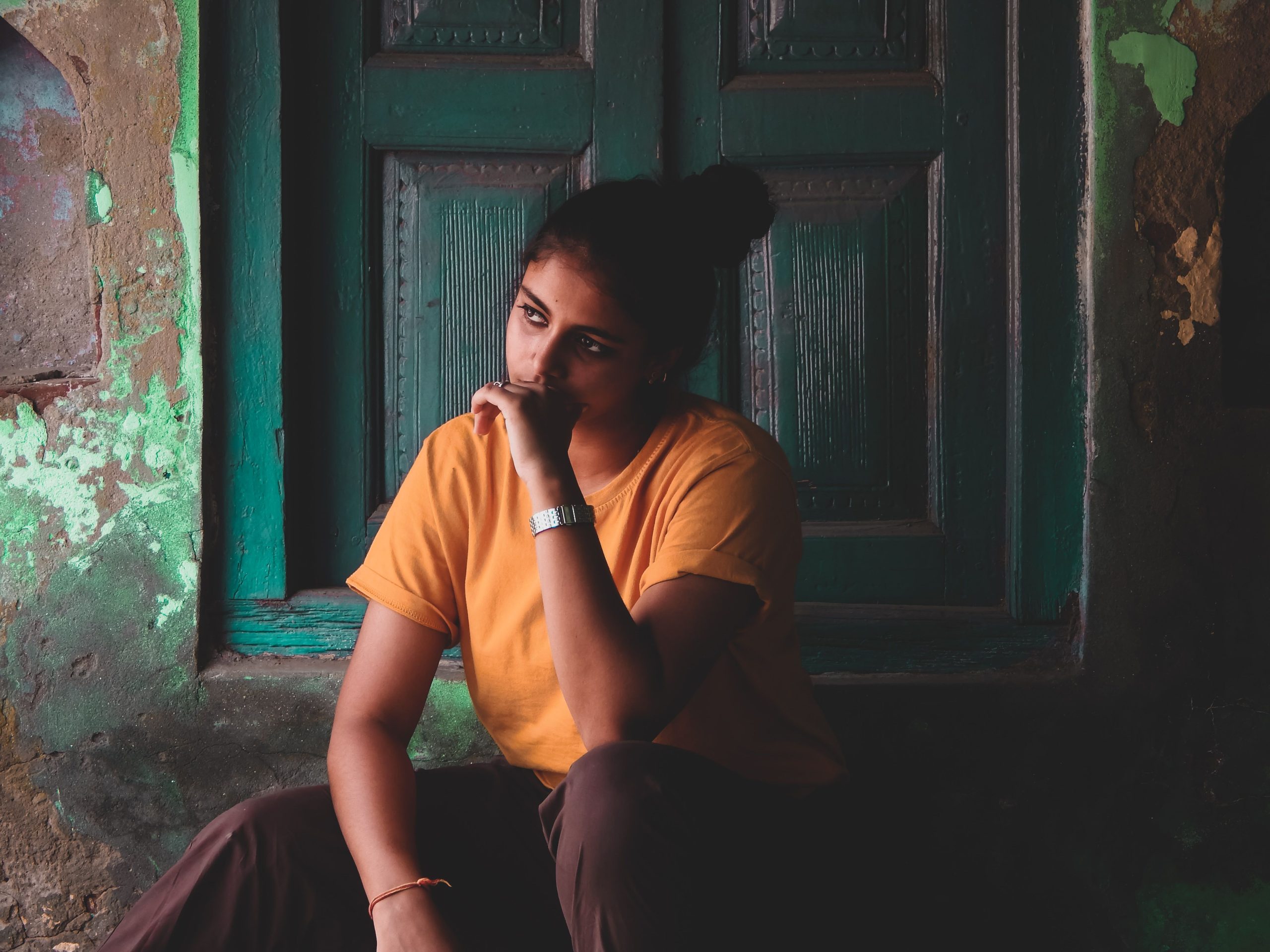 Jeune femme pensive assise devant porte turquoise